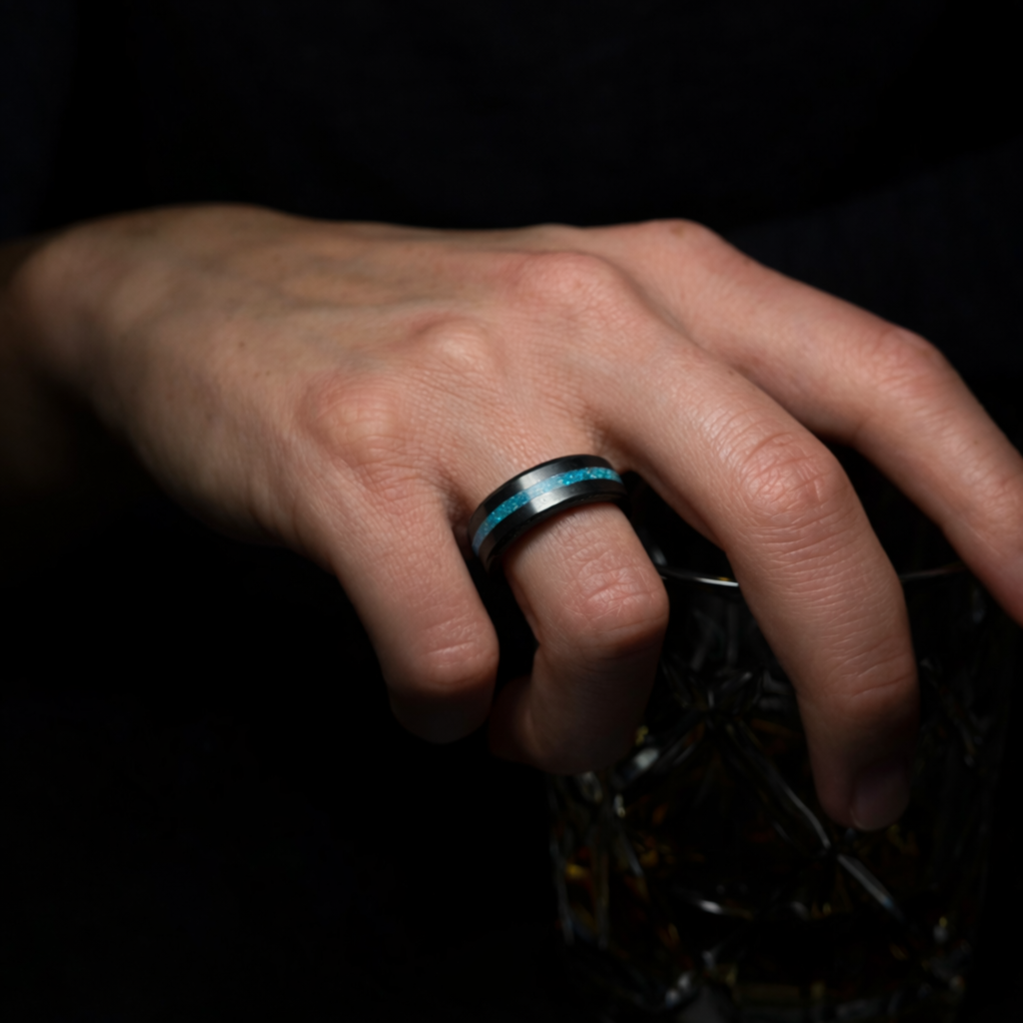 Hand wearing a solid black diamond ring with a blue opal inlay on a dark background