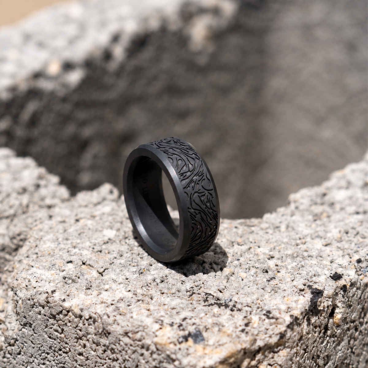 ARES solid black diamond ring with an example flowing abstract laser design, standing on textured stone.
